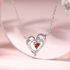 Two sleek silver dolphins gracefully arch toward each other, forming an elegant heart shape. Nestled between their arched bodies, a brilliant red heart-shaped stone, glistens with passion and devotion. As you wear this necklace, let it serve as a reminder of love's boundless possibilities.Carat Weight: 0.395 ctStone Size: 4*4 mmStone Type: Jeulia® StoneNumber of Stones: 1 Stone Shape: HeartStone Color: Garnet RedWeight: 2.1 gWidth: 15.1 mmHeight: 16.4 mmThickness: 3.1 mmMaterial: 925 SilverPlati Elegant Red Heart Necklace With Birthstone, Elegant Red Heart Birthstone Necklace, Silver Heart Necklace For Valentine's Day Formal, Silver Heart Necklace For Valentine's Day And Formal Events, Elegant Red Open Heart Necklace, Necklace Online, Buy One Get One, Sterling Silver Necklace, Red Heart