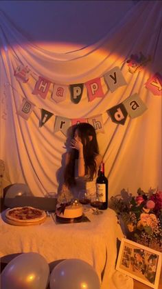 a woman sitting in front of a table with pizza and wine on it, surrounded by balloons