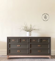 a brown dresser with drawers and a plant in the middle on top of it, against a white wall