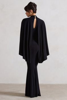 the back of a woman wearing a black dress and cape