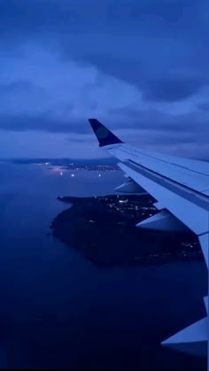 the wing of an airplane as it flies over water and land at night with city lights in the distance