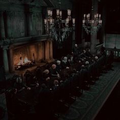 a group of people sitting around a table in front of a fire place with chandeliers