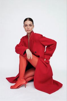 a woman sitting on the ground wearing red shoes and a long coat with an overcoat