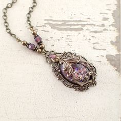 "To make this neo Victorian style necklace, I wrapped an amethyst opal glass cabochon in exquisitely detailed antiqued brass filigree. The stone is set in an antique Victorian style setting, which I embellished with matching opalescent Swarovski crystal stones. I finished the necklace with Swarovski beads, pearls, and vintage style infinity-link chain. --------------------------------------------------------------------------------------------- Dimensions and details - Focal cabochon measures 18 Art Nouveau Brass Jewelry Nickel Free, Art Nouveau Nickel-free Brass Jewelry, Elegant Bronze Cabochon Necklace, Elegant Antique Gold Cabochon Necklace, Vintage Amethyst Cabochon Jewelry, Antique Purple Metal Jewelry, Antique Bronze Necklace With Cabochon, Antique Gold Cabochon Necklace, Brass Cabochon Jewelry For Jewelry Making