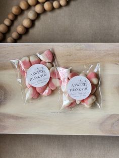 two bags of pink and white marshmallows on a wooden tray next to a bead necklace