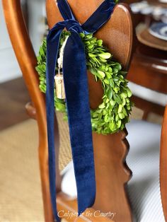 a wooden chair with a blue ribbon tied around the back of it and a wreath on top