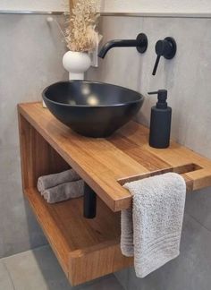 a black bowl sink sitting on top of a wooden shelf next to a white towel