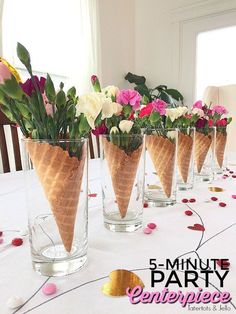 five ice cream cones with flowers in them on a white tablecloth covered dining room table