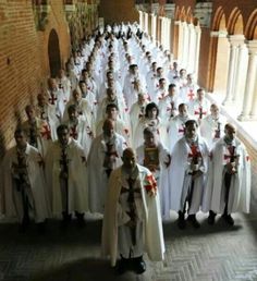 a large group of people dressed in white and wearing red crosses are lined up against a brick wall