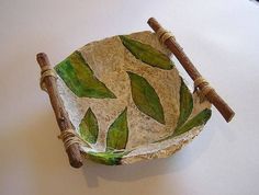 a small bowl with green leaves painted on the side and two sticks sticking out of it