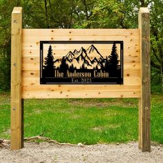 a wooden sign with mountains and trees on it in front of some green grass,