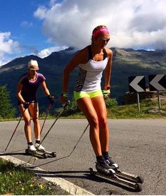 two women on skis going down the road with mountains in the backgroud