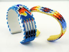 "Double Diamond Beadwork Cuff in light periwinkle blue background with red gold orange flame bead colors in a Diamond Cuff design. Oval band shape will fit a wider wrist, and is longer overall that most bead cuffs. Again this makes it ideal for a male's wrist. Length is 7 Inch Plus the opening. Adjustable Bracelet fits men women and teens. All handmade bracelets make a great holiday gift idea or birthday present. Beadwork cuff in traditional feather design and geometric patterns. Handsewn leathe Handmade Blue Beaded Bracelets For Festivals, Handmade Blue Beaded Bracelet For Festivals, Traditional Blue Beaded Bracelets For Festivals, Unique Blue Cuff Bracelet For Festival, Artisan Blue Cuff Bracelet For Festivals, Blue Beaded Bangle Cuff Bracelet, Blue Beaded Cuff Bangle Bracelet, Blue Cuff Bracelets For Festivals, Blue Cuff Bracelet For Festival