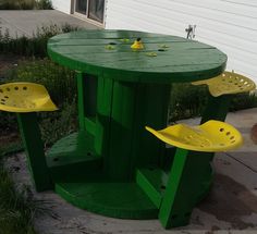 a green table with yellow plastic chairs on the top and bottom, in front of a white house