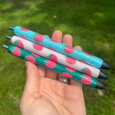 three pens with strawberries on them are held in someone's hand