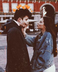 two people standing next to each other in front of a building with hearts on it