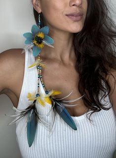 a woman wearing a white tank top with blue and yellow feathers attached to her neck