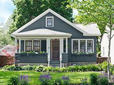 a small gray house with white trim and flowers in the front yard on a sunny day