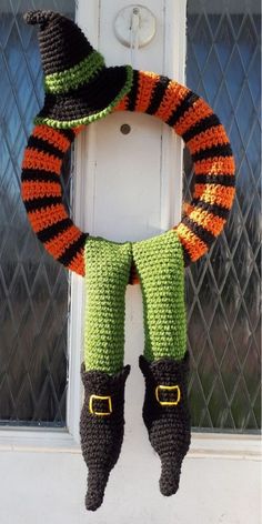 a crocheted halloween wreath hanging on the front door with boots and a hat