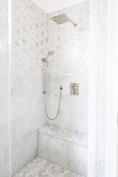 a bathroom with white marble walls and flooring, including a shower head and hand shower