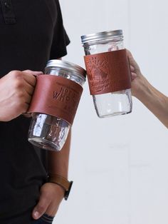 two people holding mason jars with leather labels