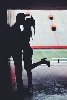 a man and woman standing next to each other in front of an empty stadium field