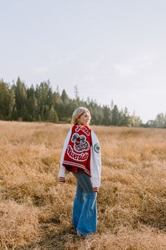 a woman standing in a field wearing a red and white jacket