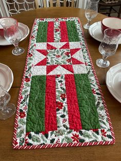 a christmas table runner on a dining room table with place settings and wineglasses