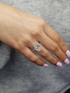 a woman's hand wearing a ring with a heart shaped diamond on the middle