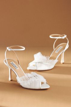 white bridal shoes with ruffles on the heel and ankle strap, sitting on a tan surface