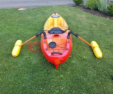 an orange and red kayak sitting on top of grass in the middle of a yard