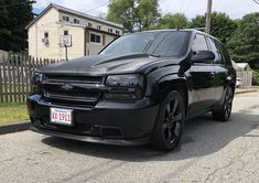 a black suv parked in front of a house on the side of the road next to a fence