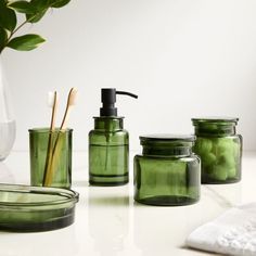 green glass containers with toothbrushes and soap dispensers on a counter