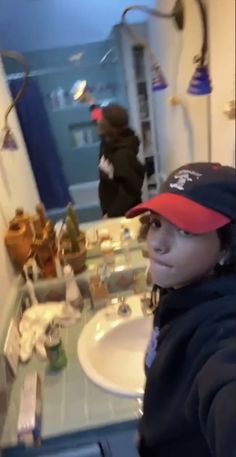 a person taking a selfie in front of a bathroom sink with other items on the counter