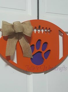 an orange football shaped sign with a bow hanging from it's side, decorated with paw prints