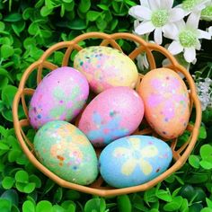 a basket filled with painted eggs sitting on top of lush green grass next to flowers