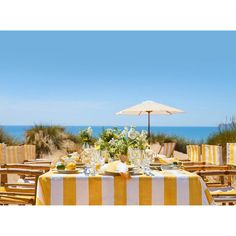 an outdoor dining table set with yellow and white striped linens for two people at the beach