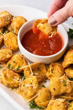 a person dipping sauce onto some fried food on a white plate with parmesan cheese