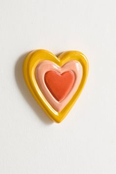 a yellow and pink heart shaped brooch sitting on top of a white table next to a wall