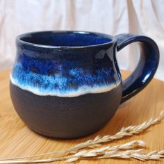 a blue and black coffee mug sitting on top of a wooden table next to some wheat