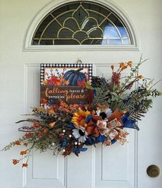 a wreath is hanging on the front door with fall flowers and pumpkins in it