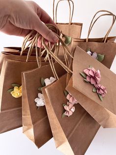 a hand is holding brown paper bags with flowers on them and string attached to the handles