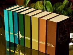 five books are lined up on a table in front of some plants and greenery