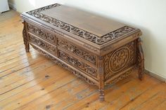 an ornate carved wooden chest sitting on top of a hard wood floor next to a white wall