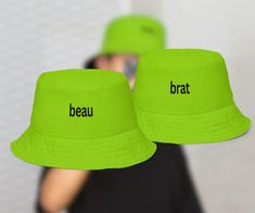 two bright green hats with the words brau and beau written on them, in front of a woman taking a selfie