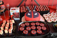 a table topped with cakes and cupcakes covered in red frosting next to a spiderman cake