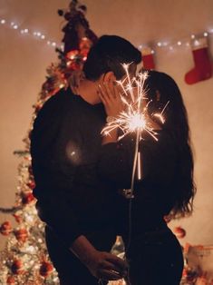 a man and woman kissing in front of a christmas tree with sparklers on it