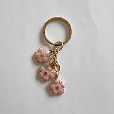 a gold keychain with pink flowers hanging from it's side on a white surface