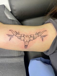 a woman's arm with a cow skull and arrows tattoo on the left forearm