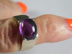 Jelly Bean Amethyst Cabochon Ring in !4K white gold. The ring features an oval amethyst that measures 12X10mm and by formula is 4.5 carats. The gemstone is set East to West and in a square top white gold mounting. The ring is solid 14K white gold and has a very good gold weight of 5.3 grams of solid gold. Currently a size 8, the ring can be sized up or down as needed. The ring is 10mm wide and tapers down to 4.85mm at bottom with a rise off of the finger of 7.29mm. Note that 6mm is approximately Modern Amethyst Ring With Polished Finish, Modern Oval Amethyst Ring With Polished Finish, Oval Amethyst Ring For Gift, Modern Oval Amethyst Ring For Gift, Modern Oval Amethyst Ring Gift, Square Top, Jelly Bean, Cabochon Ring, Alternative Engagement Rings